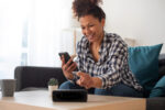 Black woman connecting phone to her virtual assistant smart speaker