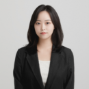 Headshot of a person with shoulder-length black hair, wearing a black blazer over a white top, against a plain background.