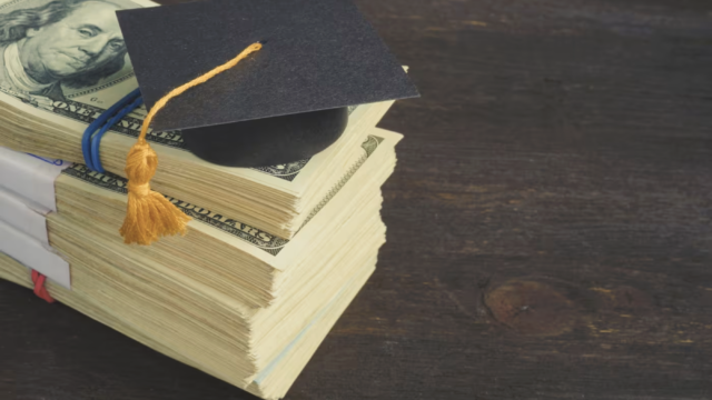 Stack of U.S. hundred-dollar bills with a black graduation cap on top, symbolizing student loans or the cost of education.