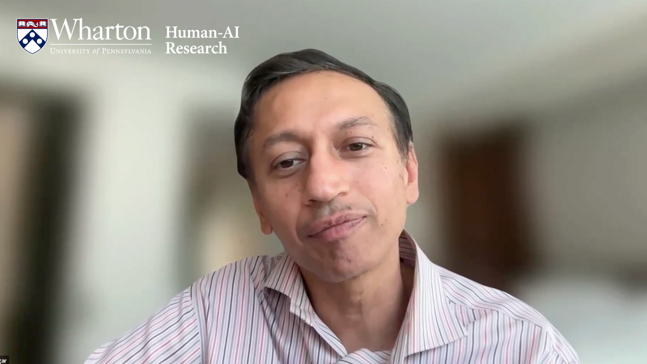 Headshot of a person wearing a striped shirt, with a Wharton School logo in the top left corner. The background text mentions Human-AI Research.