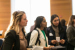 A group of individuals attentively participating in a professional or networking event, holding documents and a coffee cup, suggesting engagement and discussion.