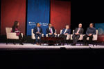 A panel discussion with six people seated on stage. They are engaged in conversation, with a backdrop displaying logos of Wharton and Working Nation.