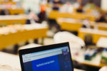 A laptop displaying a presentation titled "DATAVIZ HACKATHON" in a blurred classroom or conference setting with attendees at tables.