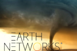 A tornado funnel touching down in an open field under dark, dramatic clouds with the logo "Earth Networks" superimposed on the image.