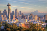 Seattle skyline with the Space Needle in the foreground, downtown skyscrapers, and Mount Rainier in the background under a clear sky.