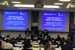 A panel discussion event in a lecture hall setting, featuring speakers on stage with a large screen displaying information about a private equity panel discussion organized by Wharton Customer Analytics Initiative and Two Six Capital. Attendees are seated, viewing the presentation.